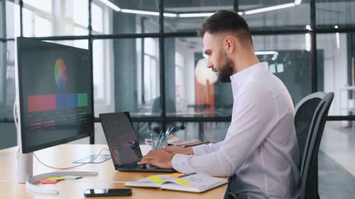 View from the side. Business person is sitting by computer in office and working.