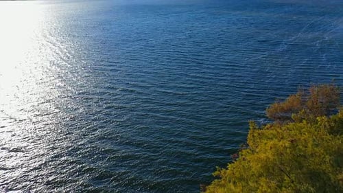 Beautiful blue lake at sunlight. Calm river near the forest with golden tree tops in autumn.