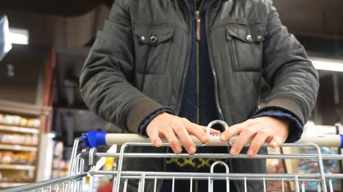 Unrecognizable Man Walking with Shopping Cart in Supermarket Guy Pushing Trolley Along Rows with