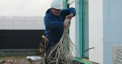 Arbeiter, der Kabel in der Nähe der Baukonstruktion verwaltet und bündelt, bereitet sich auf die technischen Arbeiten vor Ort vor Ort vor Ort vor
