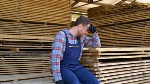 Tired Young Male Worker in Lumber Warehouse