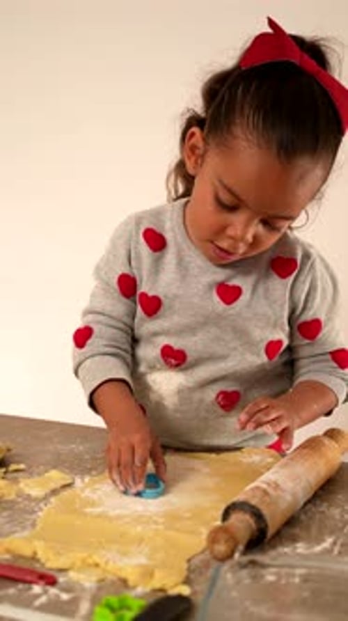 Happy girl cutting the dough to make cookies to share on Valentine's Day love and friendship