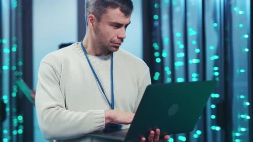 A Man Works Intently in a Server Room Managing Tasks on a Laptop
