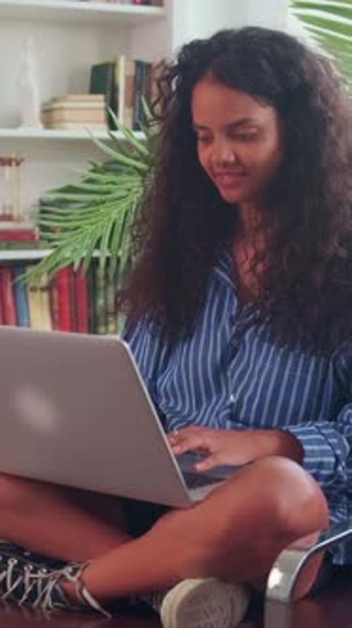 Young Woman Sitting Cross Legged on Floor Using a Laptop in a Cozy Living Room