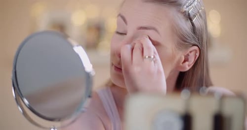 Woman Applies Makeup in Front of Mirror