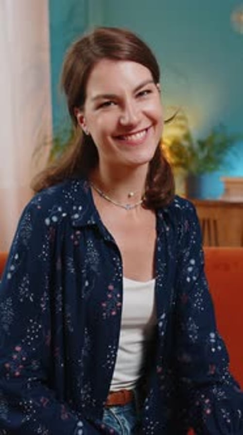 Smiling Woman With Brown Hair Sits Indoors and Smiles