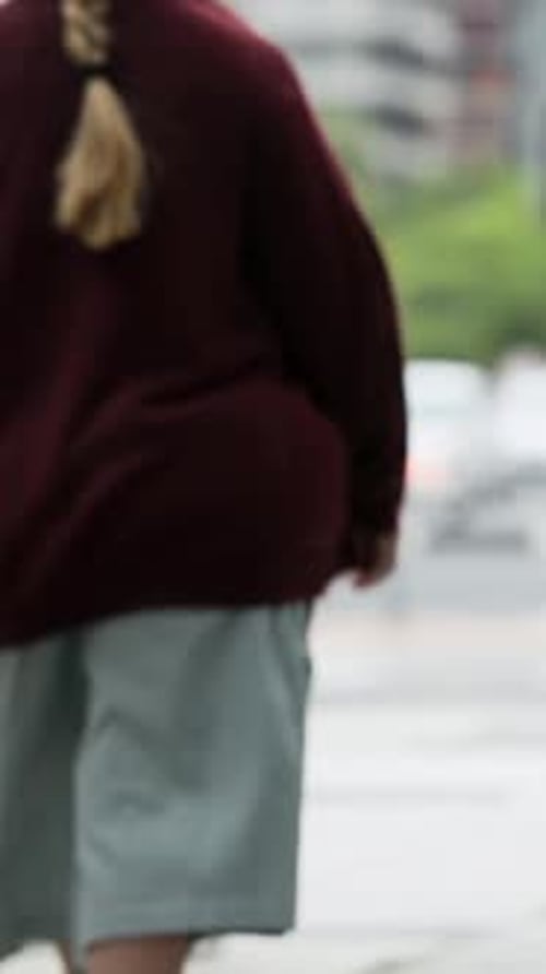 Vertical video: Crossing woman in denim jacket checking phone on street after signal with brown bag