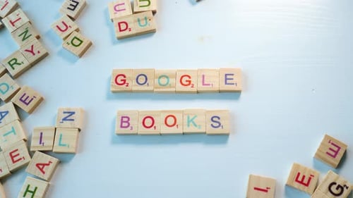 Close up of a person spelling the sentence Google Books with wooden letters on a bluish white backgr