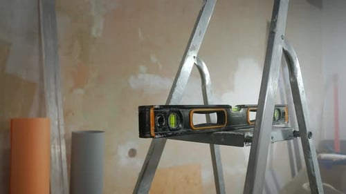 Black Water Level Lying on Metal Ladder Against Brown Wall