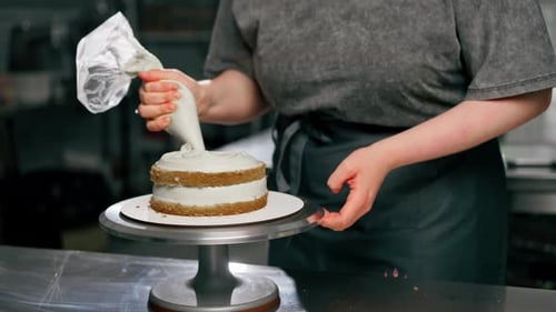Close Up Female Baker in a Professional Kitchen Puts Cream From Pastry Bag Onto a Sponge Cake