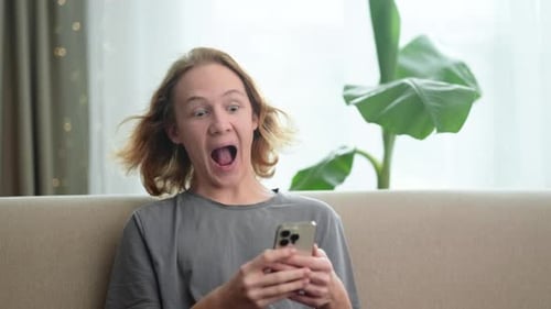 Sorprendido, sorprendido, caucásico, pelirrojo, adolescente que mira teléfono y grita emocionante con