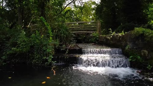 Small Wide Waterfall at the End of a Stream Coming Under a Footbridge
