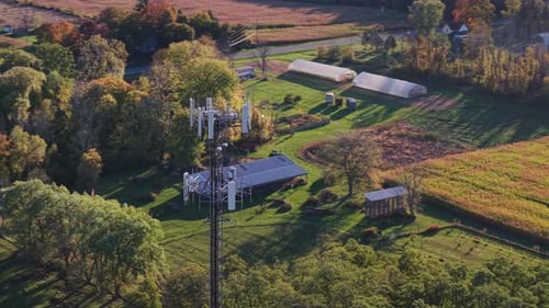 Aerial View of a Telecommunication Tower Surrounded By Farmland Green Trees and Rural Buildings