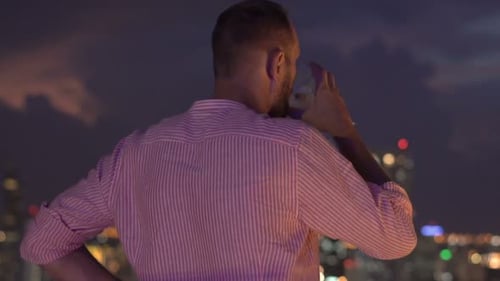 Young Man Admire Cityscape and Drinking Cocktail While Standing on Terrace At