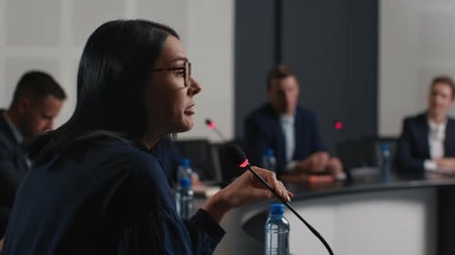 Speech Of Political Speaker At Meeting Room Of Modern Business Center. Adult Woman In Suit Explai...
