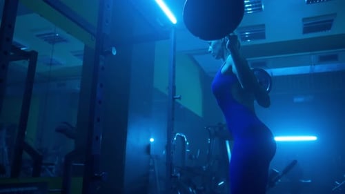 Side View of a Dark Silhouette of Woman is Squatting with Barbell in Gym with Blue Light