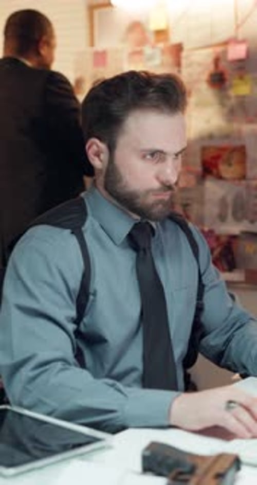 Serious Man Works at Desk with Papers and Gun
