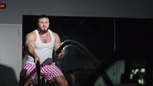Muscular Man Powering Through Intense Battle Rope Workout in an Indoor Gym Creating Powerful Rope