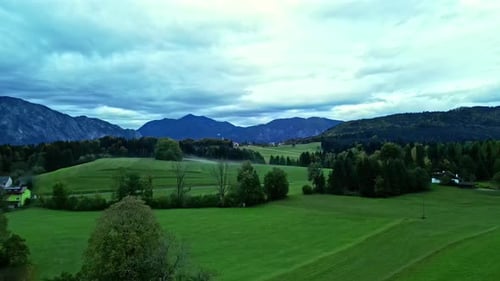 Lush green valley with mountains in the background, overcast sky, aerial view