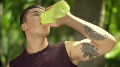 Tired Sport Man Drinks Water From Plastic Bottle After Marathon in Park