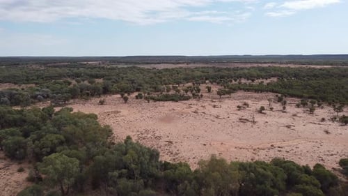 Drone flying over a remote Australian outback land with trees and some bold patches