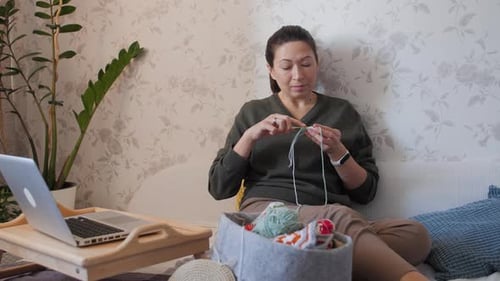 Woman Knitting with Yarn on Sofa at Home