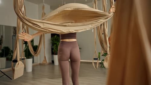 Woman Does Aerial Yoga Assisted by Instructor Indoors
