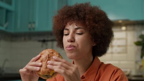 Black Woman Eating Yummy Burger Close Up 20s Female Enjoy Cheeseburger Looking at Camera