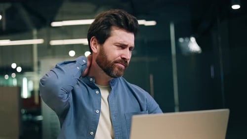 Man Massages Stiff Neck at Office Computer