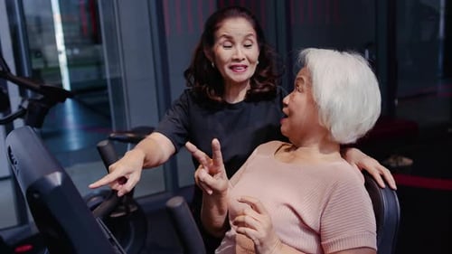 Happy senior Asian women exercising in gym, Trainer helps an elderly woman with the stationary bike