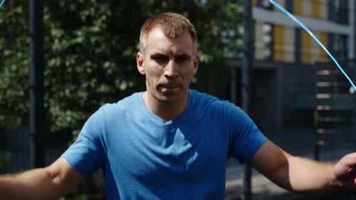 A Muscular Man in a Blue Tshirt Jumps Rope Outdoor Sports Hobbies on the Basketball Court