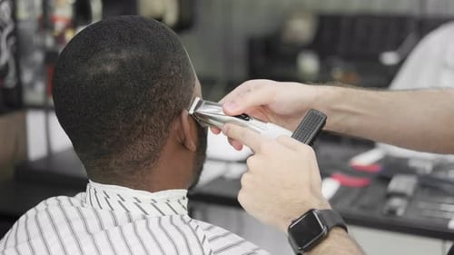 Barber cutting the hair of a young black man in a barbershop studio. Professional hairdresser cuttin