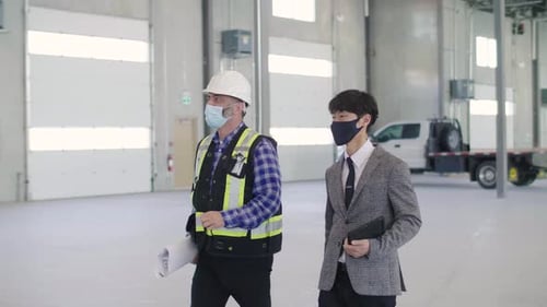 Architect and foreman in face masks inspect vacant warehouse during covid19 pandemic