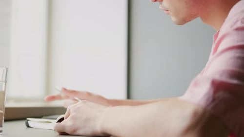 Young Adult Writing in a Notebook by Window