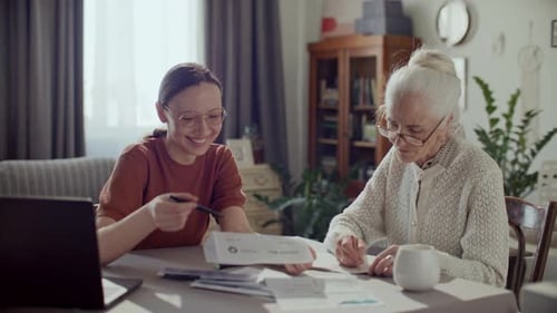 Female Caregiver Assisting Elderly Woman with Financial Documents at Home