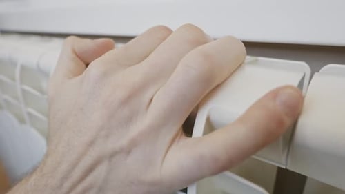 Close Up Male Hand Checking Central Heating Radiator At Home