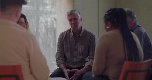 Man speaks emotionally during group therapy session, surrounded by peers in quiet circle