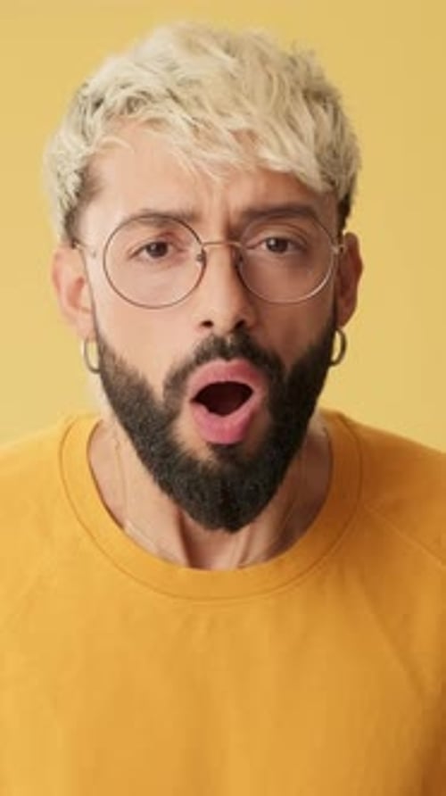 Man looking at camera with big eyes, says wow, isolated on yellow background in studio