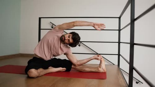 Young Man Stretching Leg on Yoga Mat Indoors