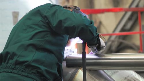 Skilled welder using TIG welding machine inside workshop, wearing mask. He is welding the stainless