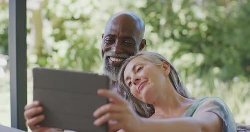 Casal sênior diversificado se inclinando atrás de uma mulher estendendo o tablet, visualizando conteúdo na varanda