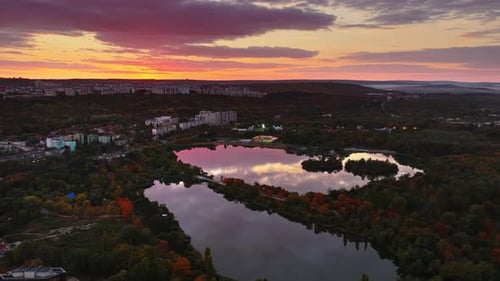 Aerial drone view of a lake reflecting the colorful evening sky and surrounding cityscape, capturing