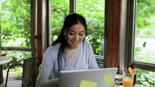 Young Asian woman working in coffee shop using laptop.