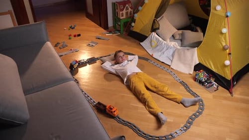 Boy Lying Around a Toy Train Set at Home