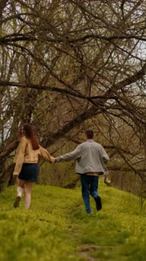 A young couple holding hands run through the forest, embodying an active lifestyle and tourism. Spor