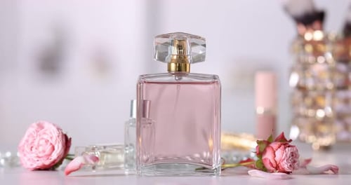 Petals falling onto bottles of perfume and beautiful flowers at white table