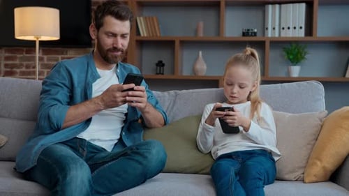 Father and Daughter on Couch Using Smartphones