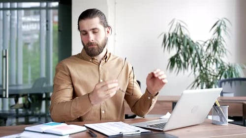 Man Tired, Rubs Eyes at Office Desk