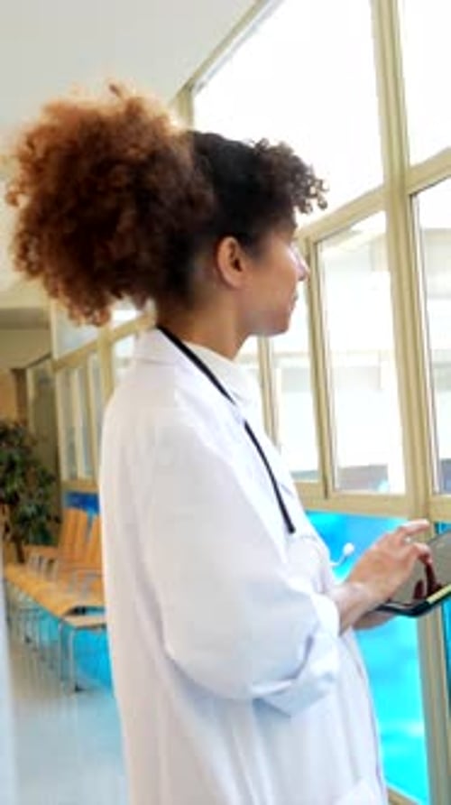 Doctor Using Tablet While Talking to Patient in Hospital Corridor