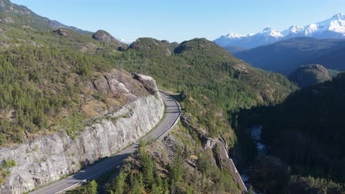 Rodovia panorâmica de montanha serpenteando pelas exuberantes florestas da Colúmbia Britânica em direção a picos cobertos de neve, pode